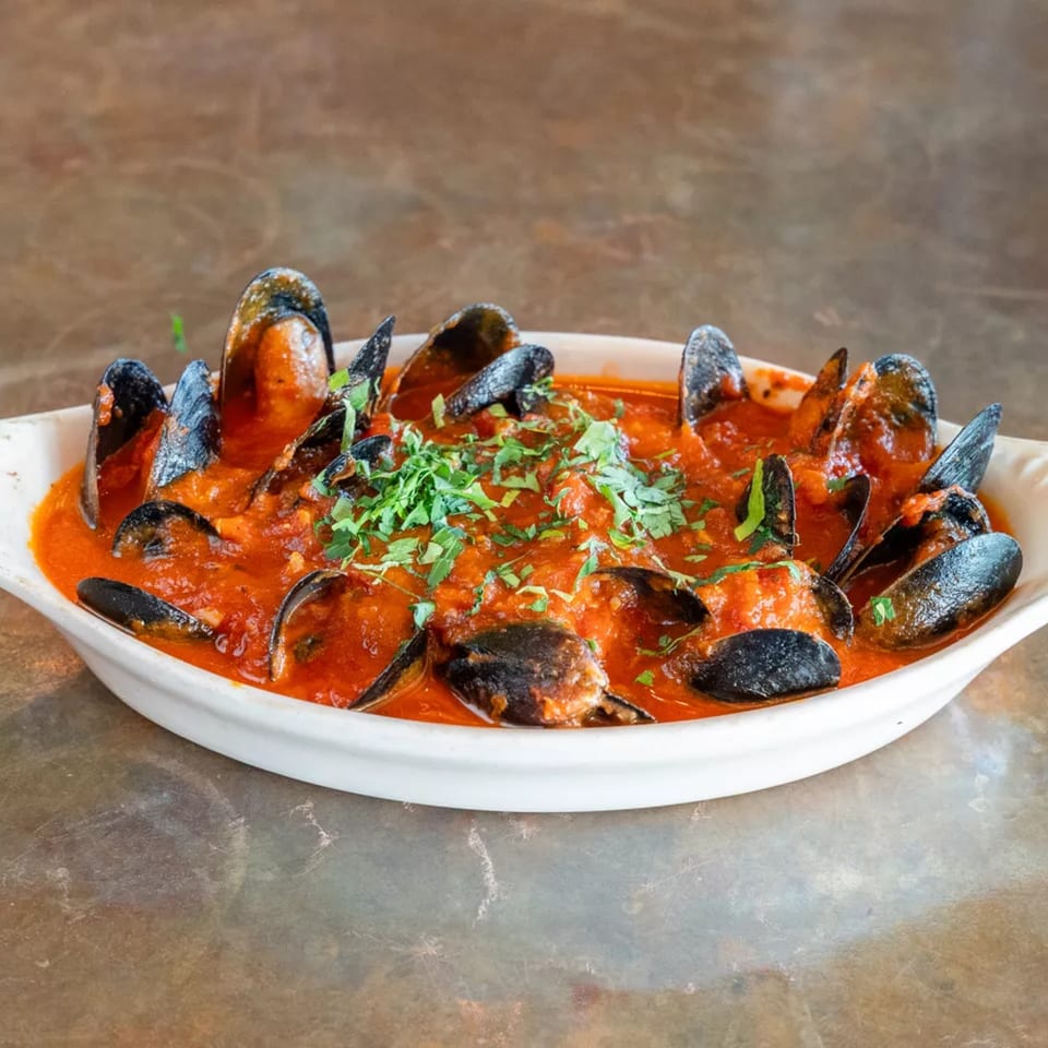 Mussels in a rich red tomato sauce, garnished with fresh parsley, served in a white dish.