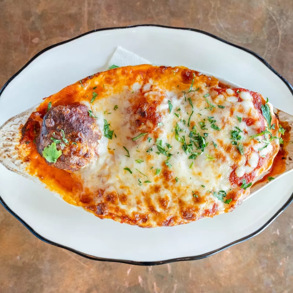 Baked meatballs in marinara sauce with melted mozzarella cheese and fresh parsley in a white dish.